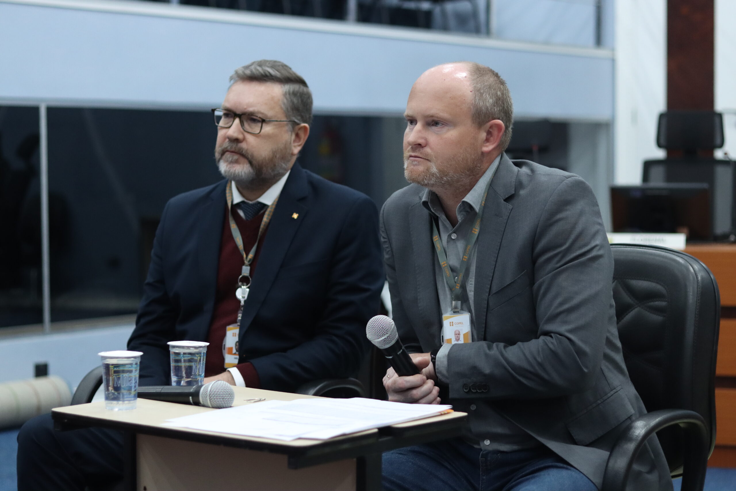 Dois homens representantes da Copel sentados em cadeiras ouvindo perguntas